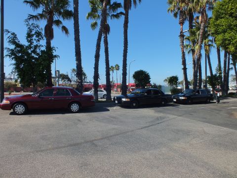 2003 Ford Crown Victoria - Dark red sedan and two black sedans angled across an empty lot under blue sky