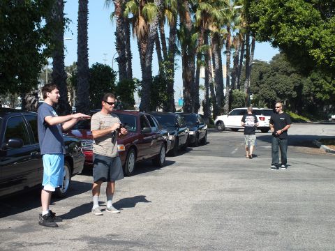 2003 Ford Crown Victoria - Group conversing near queued sedans, white pickup and another man in the background
