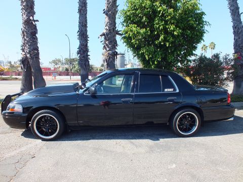 2003 Ford Crown Victoria - Dark sedan parked sideways with port cranes and storage tanks behind it