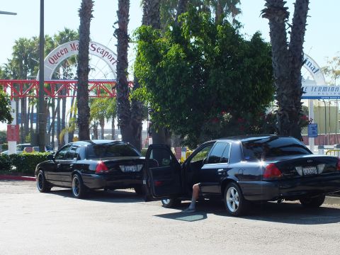 2003 Ford Crown Victoria - Black sedans, one with door open, in front of the red Queen Mary Seaport sign