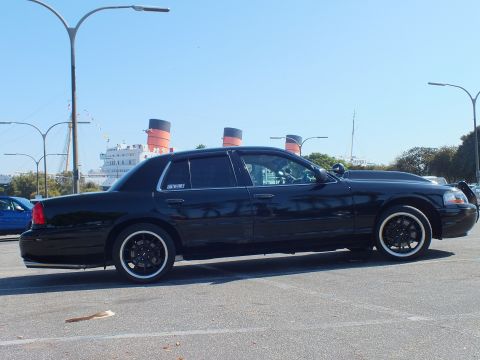 2003 Ford Crown Victoria - Lowered black full-size sedan on whitewall tires with the ocean liner's red funnels behind