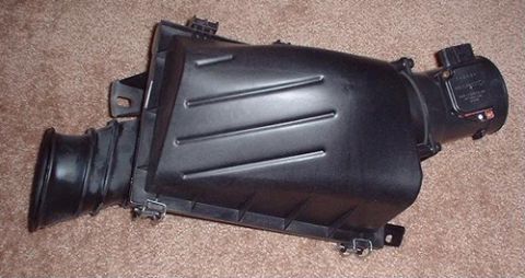 1998 Ford Crown Victoria - black plastic automotive air cleaner airbox with an inlet snorkel and mounted air-flow sensor, sitting on carpet.