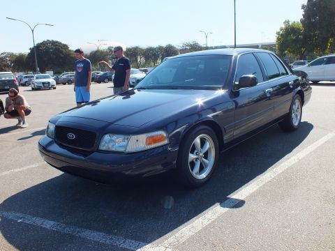 2003 Ford Crown Victoria - Navy Ford full-size sedan on machined alloy wheels with people standing behind it