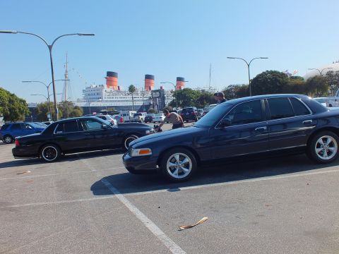 2003 Ford Crown Victoria - Navy sedan on alloy wheels in foreground with a black sedan and the ship beyond