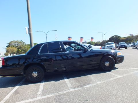 2003 Ford Crown Victoria - Black sedan shown in profile with black steel wheels, ship funnels and parked cars filling the background.