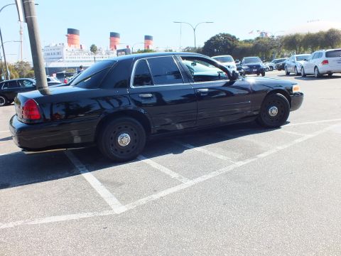 2003 Ford Crown Victoria - Rear quarter of a black full-size sedan on plain steel wheels, the liner's funnels rising past the lot.