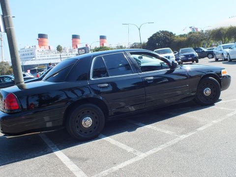 2003 Ford Crown Victoria - Black four-door sedan in profile with dark steel wheels, ship funnels and cars across the striped lot.