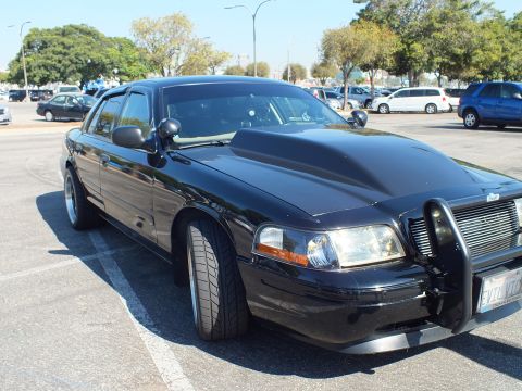 2003 Ford Crown Victoria - Lowered black Crown Victoria with chrome grille and steel push bar, California plate, parked under blue sky.