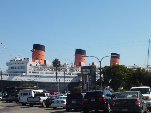 2003 Ford Crown Victoria - Orange-and-black funnels of the moored liner rise above parked sedans, an SUV and a small bus.