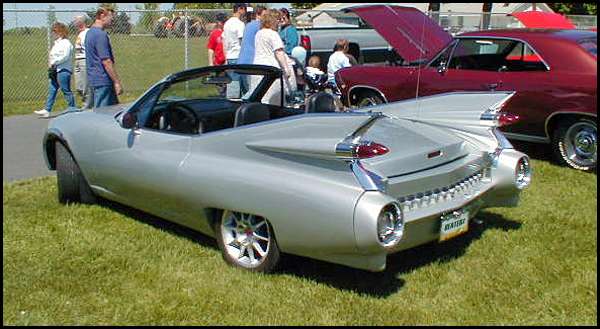 Silver custom convertible with tall tailfins and round taillights at outdoor car show
