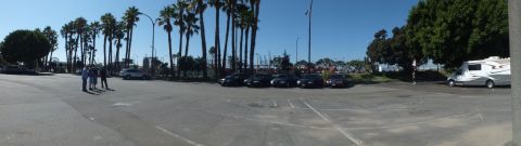 2003 Ford Crown Victoria - Panorama of a port-side lot showing a sedan lineup, scattered palms, an RV and a few standing people.