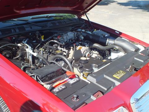 2003 Ford Crown Victoria - Open engine bay of a red Ford sedan, exposing the V8 intake, accessory belt and yellow caution label.