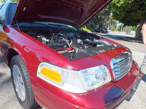 2003 Ford Crown Victoria - Front three-quarter of a maroon Crown Victoria, hood raised over the engine, chrome grille and alloy wheel.