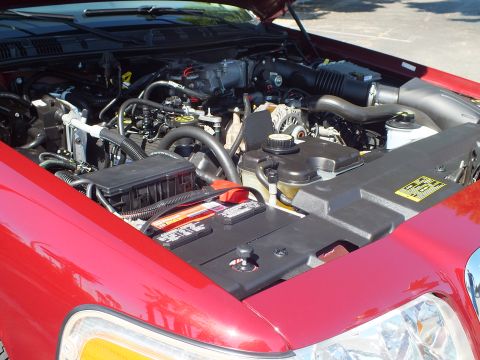 2003 Ford Crown Victoria - Close-up under the hood of a red Ford sedan showing the V8 engine, alternator, intake and emissions label.