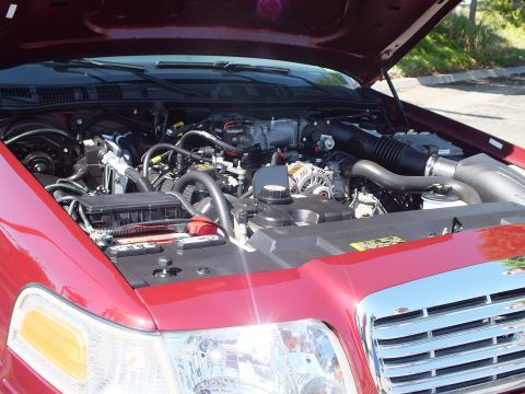 2003 Ford Crown Victoria - Under-hood angle of a maroon Ford sedan showing the V8 engine above the chrome grille and headlight.