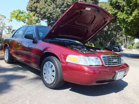 2003 Ford Crown Victoria - Dark red Ford Crown Victoria parked with open hood, showing chrome grille and silver hubcaps.
