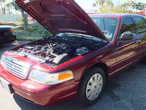 2003 Ford Crown Victoria - Dark red Ford Crown Victoria sedan with raised hood, sun glinting off the chrome grille.