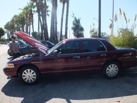 2003 Ford Crown Victoria - Side view of a dark red Ford Crown Victoria with hood raised in a palm-lined coastal lot.