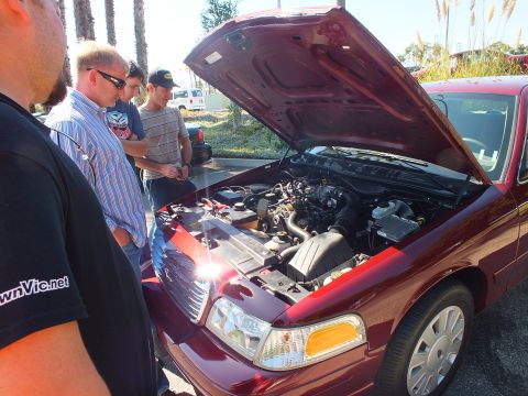 2003 Ford Crown Victoria - Men gathered around a dark red Ford Crown Victoria engine bay; one shirt reads CrownVic.net.