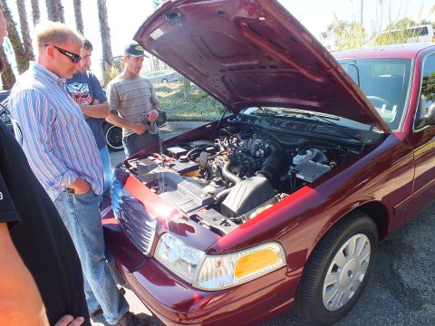 2003 Ford Crown Victoria - Several men examine the V8 engine of a dark red Ford Crown Victoria with the hood raised.