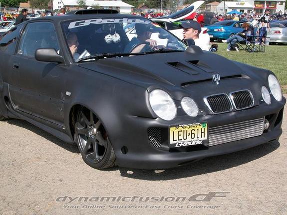 Matte black modified coupe, 3/4 front view, custom bumper, hood scoop, intercooler, car show