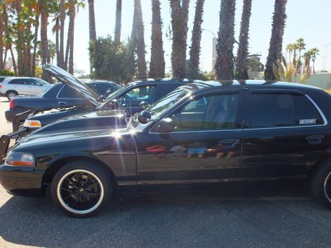 2003 Ford Crown Victoria - Side profile of a blacked-out Crown Victoria, hood open, parked under palms at a car meet.