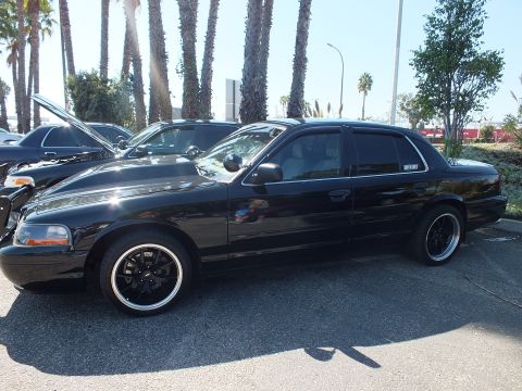 2003 Ford Crown Victoria - Profile of a black Ford sedan on gold-lip black wheels, parked at an outdoor show.
