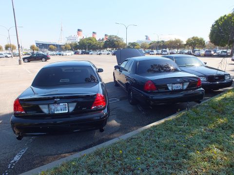 2003 Ford Crown Victoria - Pair of black Crown Victorias parked side by side with the Queen Mary in the distance.