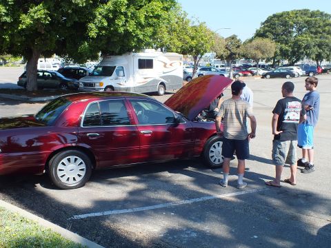 2003 Ford Crown Victoria - Dark red Crown Victoria with raised hood as bystanders inspect the engine bay.