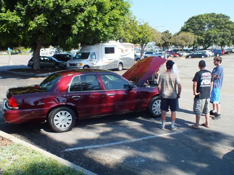 2003 Ford Crown Victoria - Rear-quarter view of a maroon Crown Victoria, hood raised, group examining it.