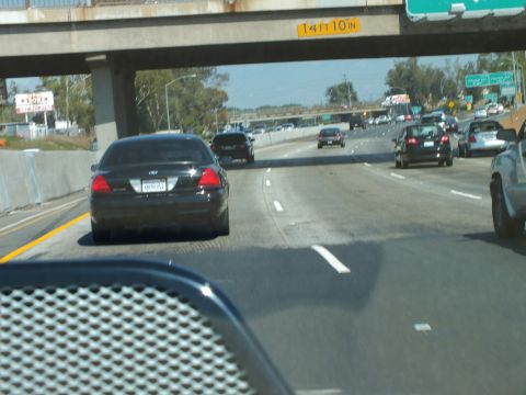 2003 Ford Crown Victoria - Black Crown Victoria seen ahead on a multi-lane freeway passing under a low overpass.