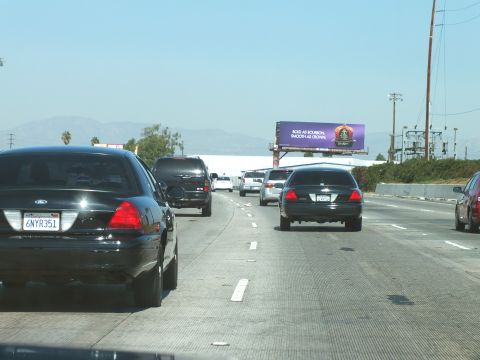 2003 Ford Crown Victoria - Black Crown Victoria with plate 6NYR351 amid freeway traffic and distant hills.