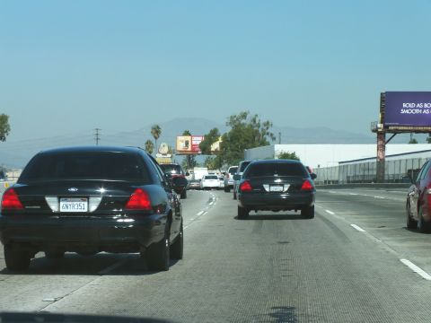 2003 Ford Crown Victoria - Black Crown Victorias rolling through freeway traffic, plate 6NYR351 in the lead.