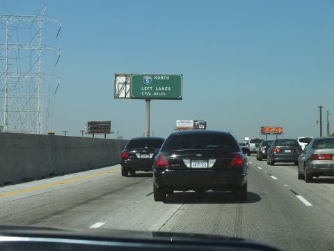 2003 Ford Crown Victoria - Black Crown Victoria ahead on I-5 North below an exit sign, mountains in the haze.