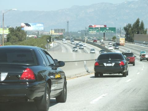 2003 Ford Crown Victoria - Black sedans merge along an open highway lined with green road signs