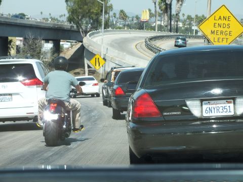 2003 Ford Crown Victoria - motorcycle rider waits beside a black sedan at a freeway merge point