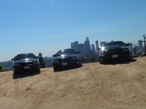 2003 Ford Crown Victoria - Sunlit black sedans staged on a hill above hazy downtown Los Angeles
