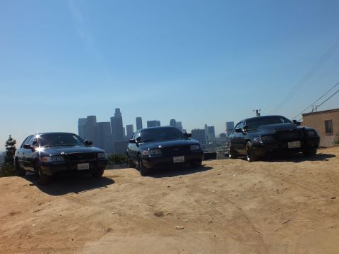 2003 Ford Crown Victoria - Black sedans parked on a hill near a building with downtown in the haze