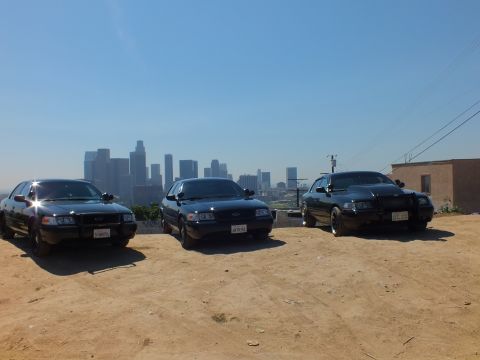 2003 Ford Crown Victoria - Black sedans lined up on a hilltop near a building above downtown