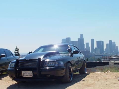 2003 Ford Crown Victoria - Customized black Crown Victoria parked on a dirt lot, push bar grille and EVIL VTC California plate, LA towers in haze