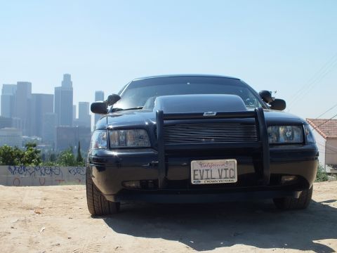 2003 Ford Crown Victoria - Head-on shot of a blacked-out Ford sedan, EVIL VTC plate in a Ford Crown Victoria frame, LA skyline at left