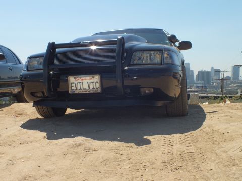 2003 Ford Crown Victoria - Ground-level shot of a black Ford sedan, push bar and EVIL VTC plate in a Crown Victoria frame, skyline at right