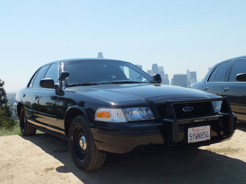 Black Ford Crown Victoria front three-quarter with steel wheels, plate 5YWN854, LA skyline