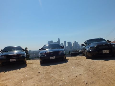 2003 Ford Crown Victoria - Three blacked-out Ford sedans face the camera on a hilltop, the right one with push bar, skyline behind