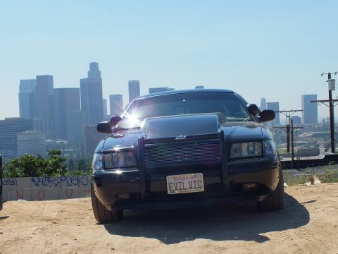 2003 Ford Crown Victoria - Black Crown Victoria front end with billet grille and brush guard; EVIL VIC plate, graffiti wall at left.