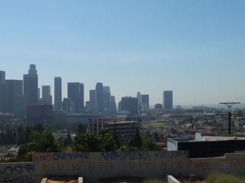2003 Ford Crown Victoria - Hazy downtown LA skyline viewed over a concrete retaining wall sprayed BURNOUTS in red graffiti.