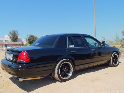 2003 Ford Crown Victoria - Lowered black Crown Victoria shown from the rear quarter on black wheels, stucco buildings behind.