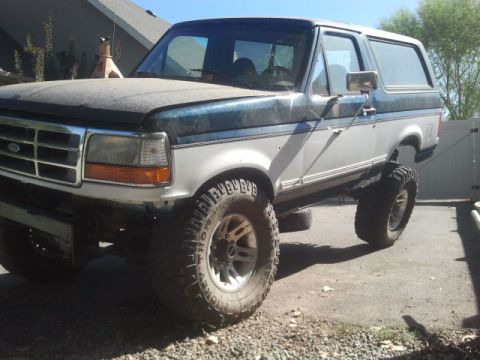1994 Ford Bronco - This lifted 1994 Ford Bronco features a two-tone paint scheme and aftermarket wheels, viewed from the front three-quarter angle.