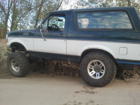 1994 Ford Bronco - Side view of a 1994 Ford Bronco with lifted suspension and large tires, partially on dirt.