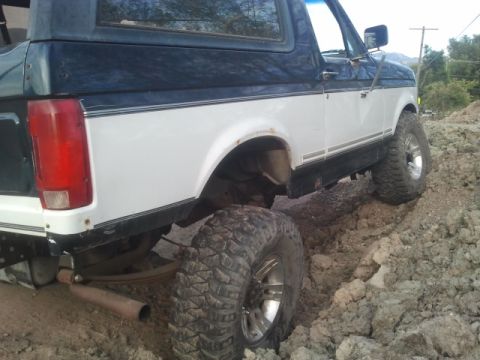 1994 Ford Bronco - This lifted Ford Bronco is navigating a rough, muddy terrain with its large off-road tires.
